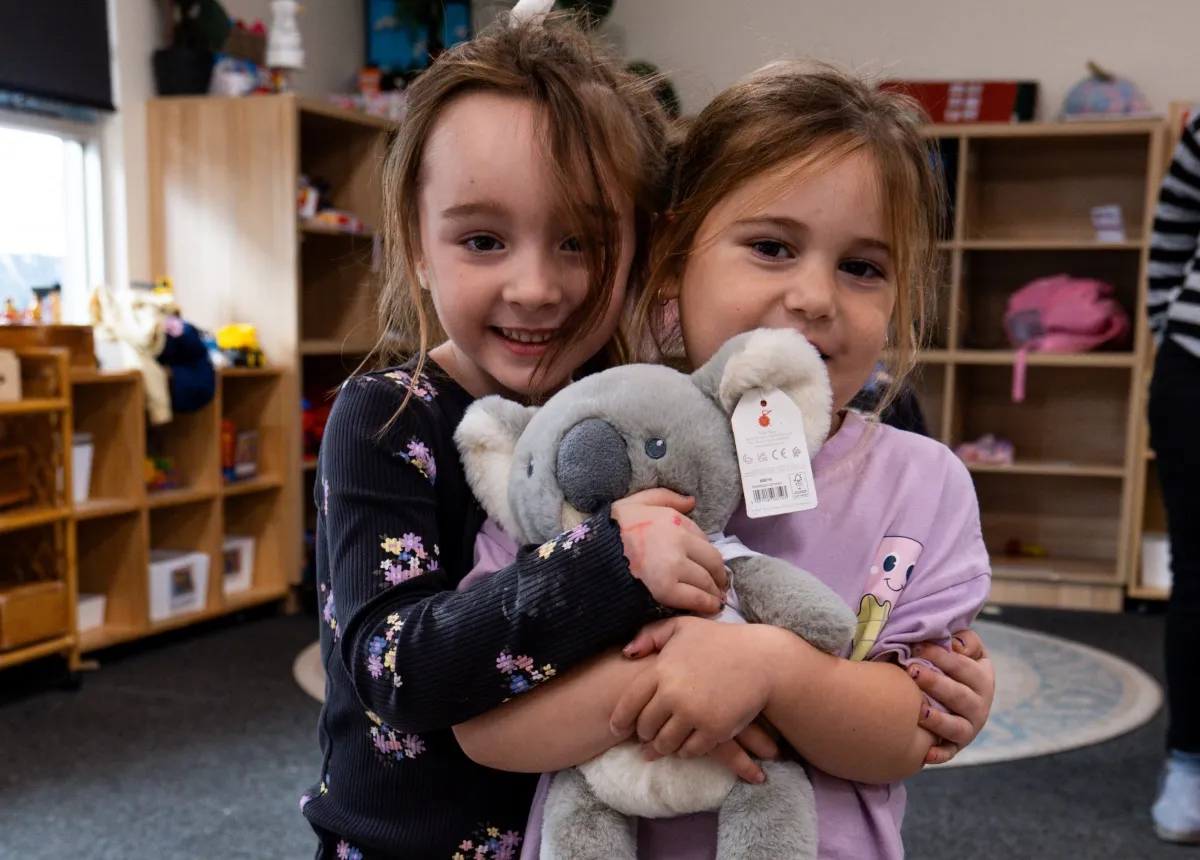 Two children hugging a Cozy Koala soft toy in their early learning room