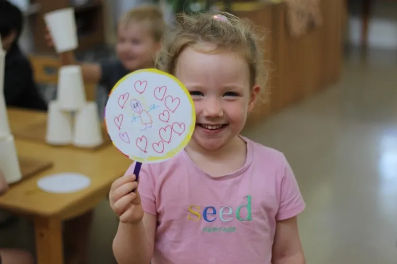 A child holding up a hand-decorated paper fan
